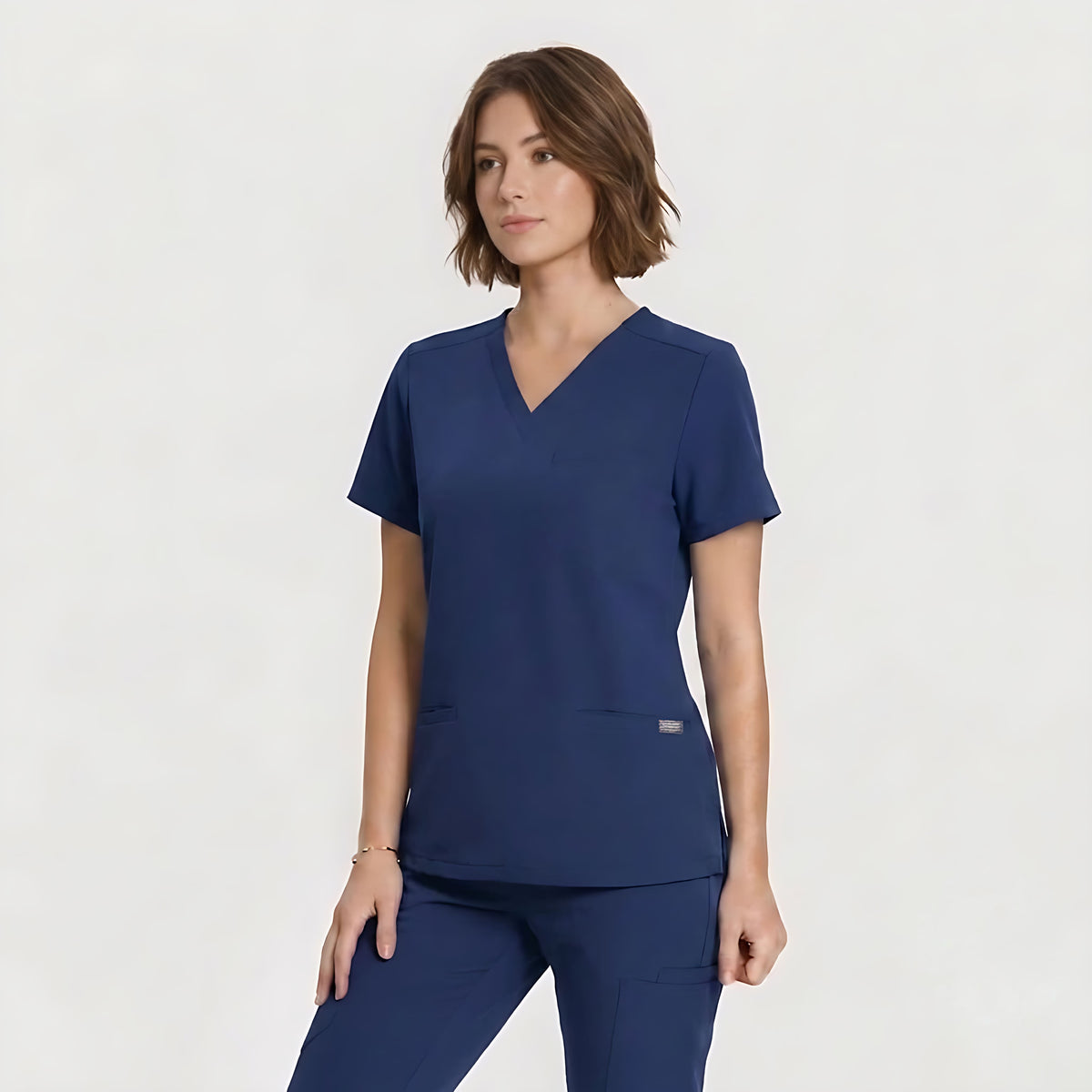 A woman modeling a navy blue scrub top and matching scrub pants against a clean, light gray studio background.