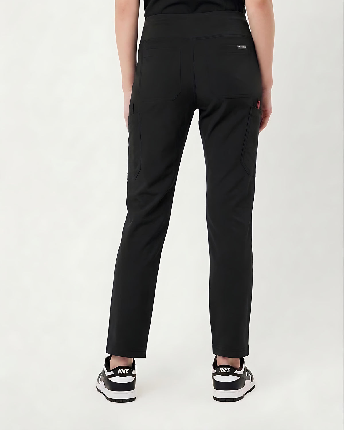 Rear view of a person wearing black cargo-style pants with side pockets and black sneakers against a plain light background.
