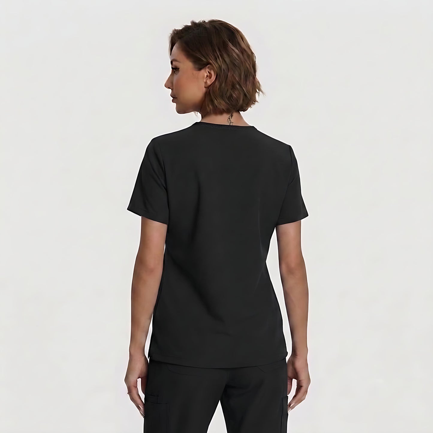 A woman with short brown hair is shown from the back wearing a plain black short-sleeve crewneck top and black pants against a light gray studio background.