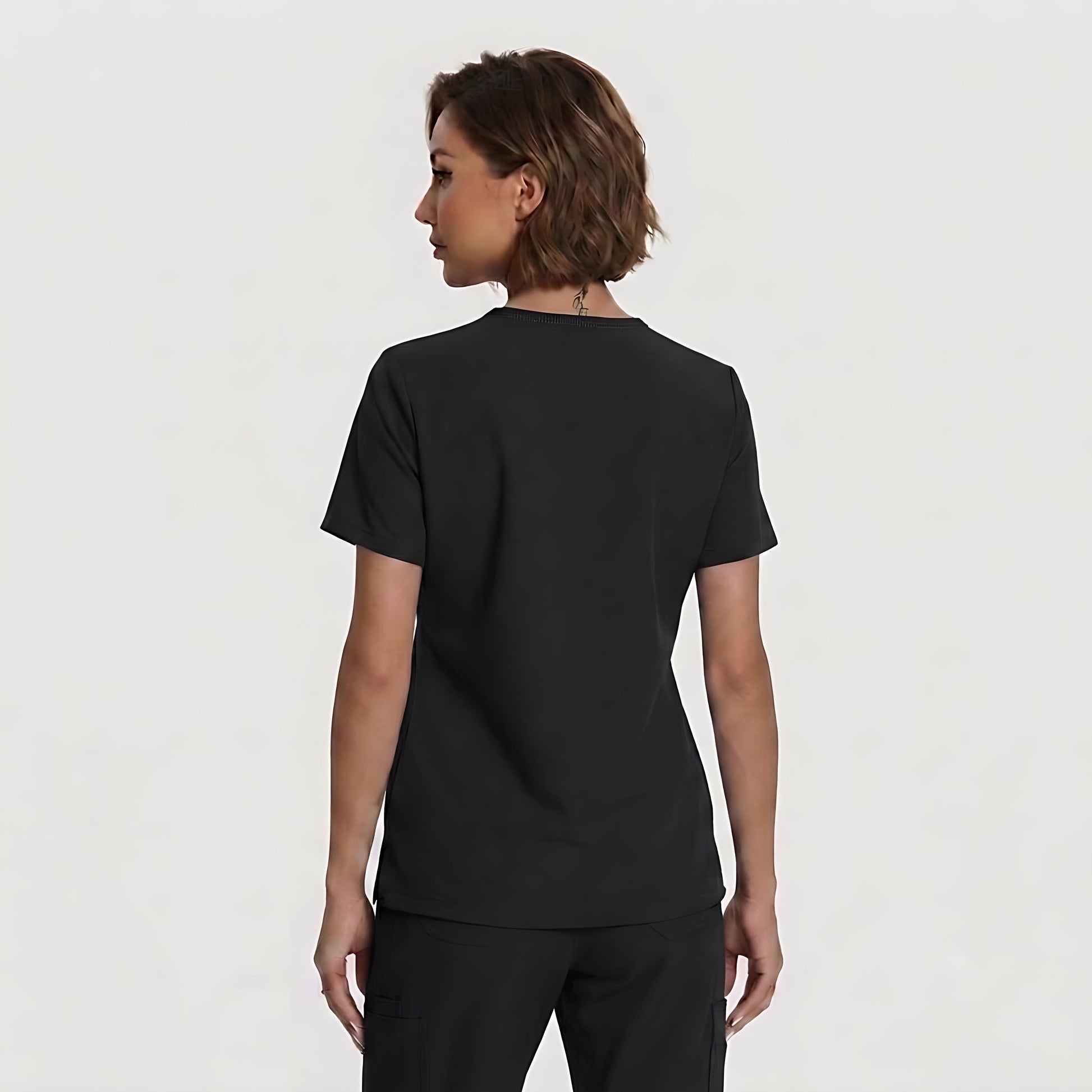 A woman with short brown hair is shown from the back wearing a plain black short-sleeve crewneck top and black pants against a light gray studio background.