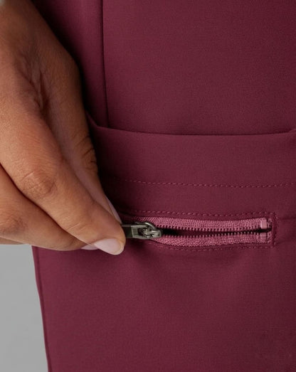 Close-up of a hand zipping a burgundy garment.