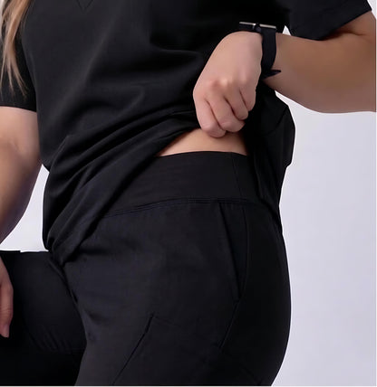A close-up of a person wearing black athletic scrub pants and a matching black top, lifting the hem of the top to show the fit and waistband.