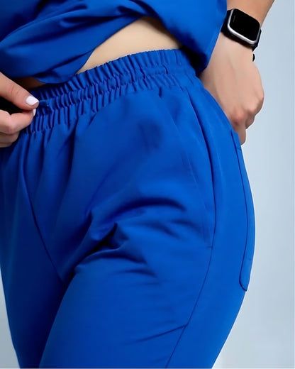 Close-up of a person wearing bright royal blue jogger-style pants with an elastic waistband, shown from the torso down against a light gray background.