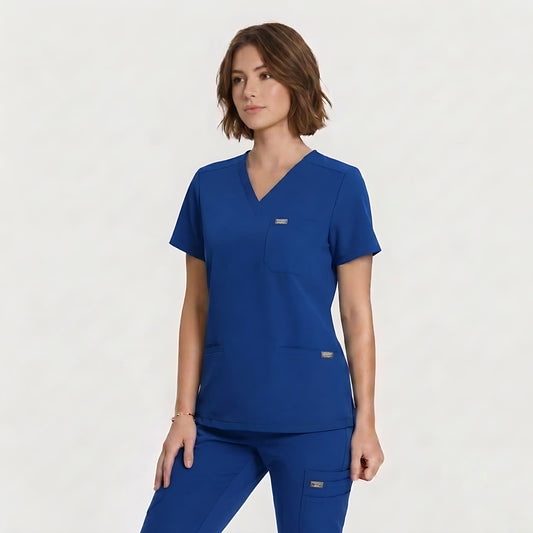 A woman modeling a royal blue scrub top and matching scrub pants against a clean, light off-white studio background.