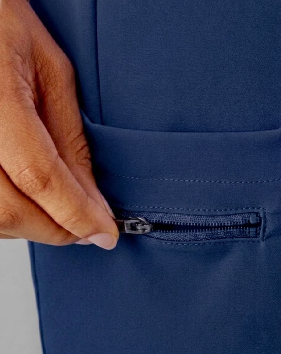 Close-up of a hand unzipping a front pocket on a navy blue garment, showing the fabric texture and zipper detail.