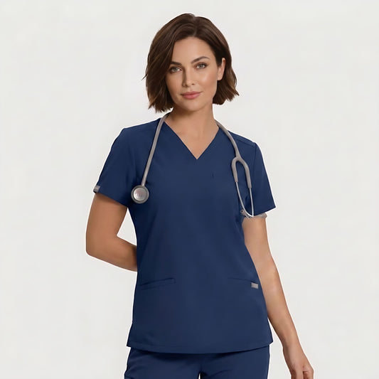 A woman wearing a navy blue V-neck scrub top and matching scrub pants, with a gray stethoscope around her neck, photographed against a light gray studio background.