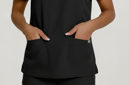 A close-up of a navy blue scrub top worn by a model, showing the front pockets with hands inserted, against a light gray background.