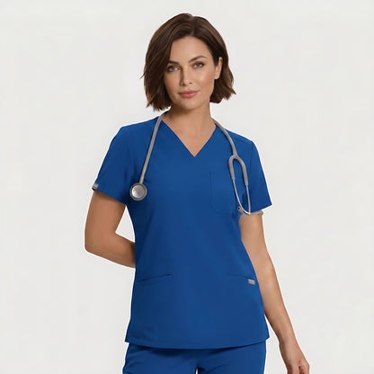 A woman wearing a royal blue V-neck scrub top and matching scrub pants, with a gray stethoscope around her neck, photographed against a light gray studio background.
