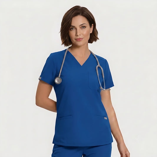 A woman wearing a royal blue V-neck scrub top and matching scrub pants, with a gray stethoscope around her neck, photographed against a light gray studio background.